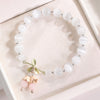 Close up of white cat's eye beads with a gold flower charm and pink crystal dangles