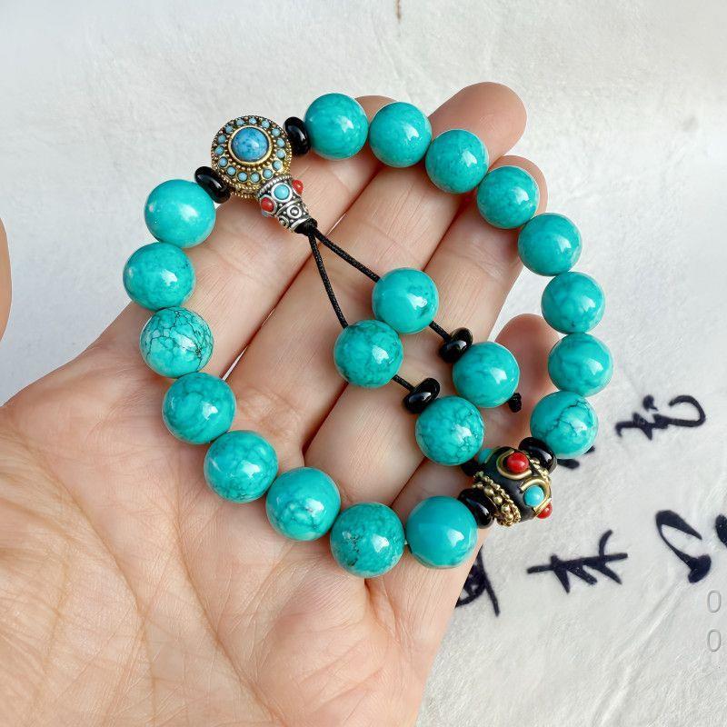Hand holding a string of bright turquoise beads with a decorative guru bead and tassels