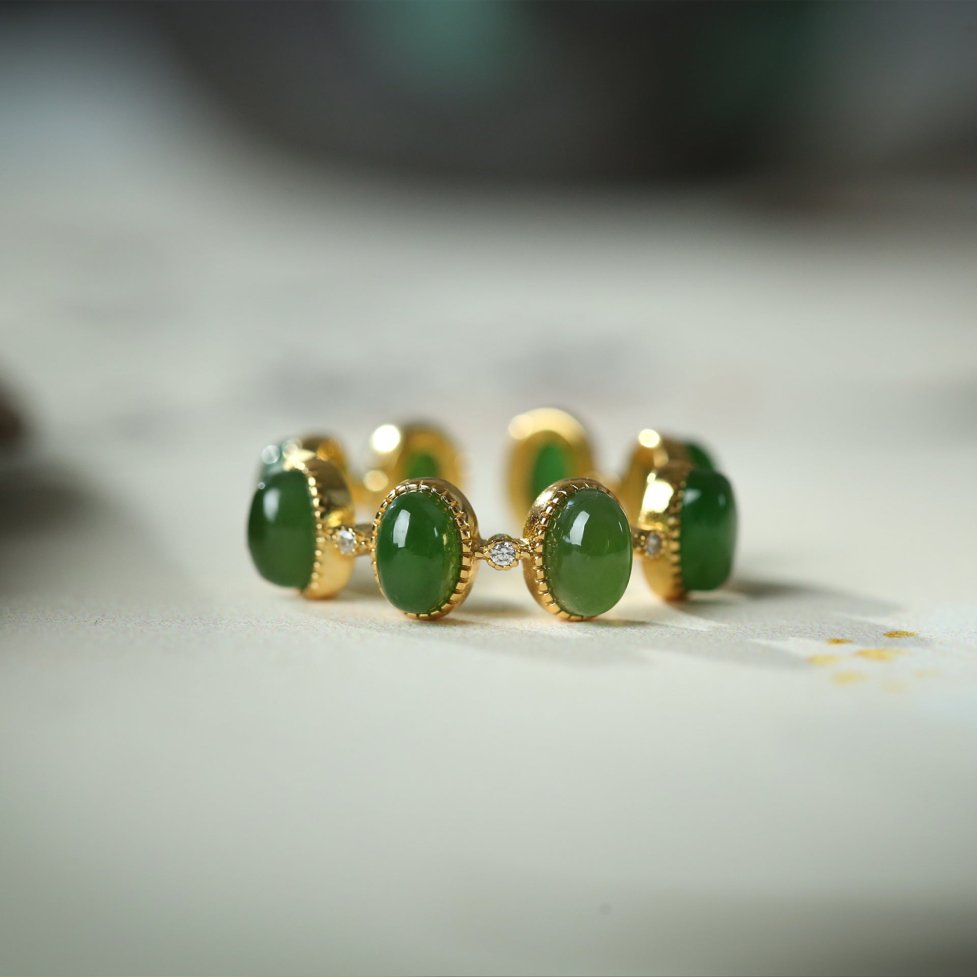 Close up of a silver ring with green stones on a white surface