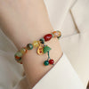 A close up of a multicolored peacock agate beaded bracelet with a gold charm on a wrist