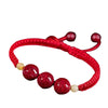 A red cord bracelet featuring three round red cinnabar beads and small accent beads