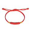 Close up of a red braided cord bracelet with gold accents on a white background