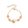 Close up of a wrist wearing a gold tone bracelet with red agate beads and a white flower center