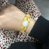 Gold tone bangle with a green jade center stone and flower carvings on a book page