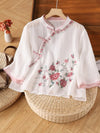 White vintage style women's shirt with pink floral embroidery and frog buttons hanging on a wooden hanger