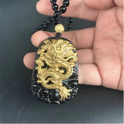 Close-up of a hand holding a black obsidian pendant with a raised gold dragon design