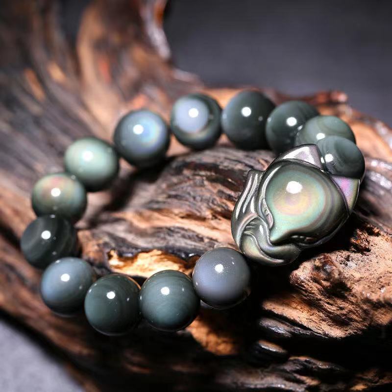 Close up view of a rainbow obsidian beaded bracelet with a carved fox charm