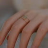 Close up of a hand wearing a double layer gold tone ring with a small green stone