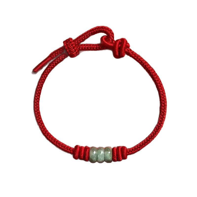 Close up of a red braided cord bracelet with three small green jade beads in the center