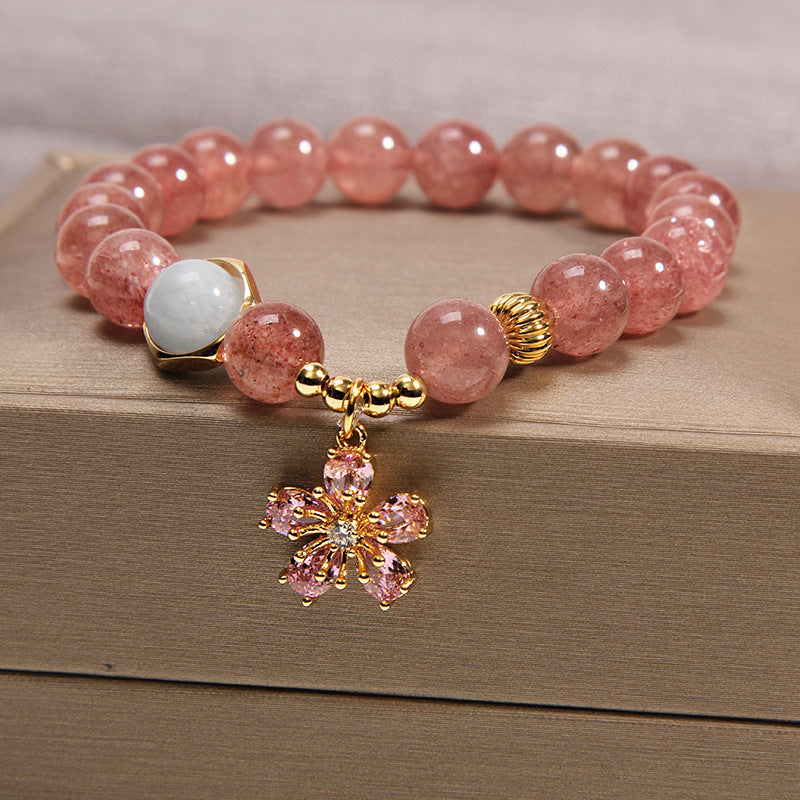 Pink strawberry quartz beaded bracelet with a gold flower charm on a wooden surface
