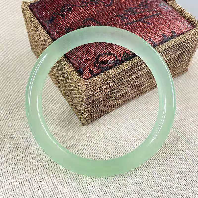 A translucent light green quartzite jade bangle resting on a textured box.