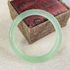 A translucent light green quartzite jade bangle resting on a textured box.