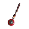 Close up of a round red cinnabar pendant with a metal wheel design and blue stone center