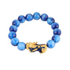 Close-up of a purple beaded bracelet with a gold Pixiu charm on a reflective surface