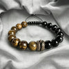Close up of a beaded bracelet with a metal snake charm on white fabric