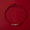 Close up of a red braided cord bracelet with a silver bamboo charm on a red background