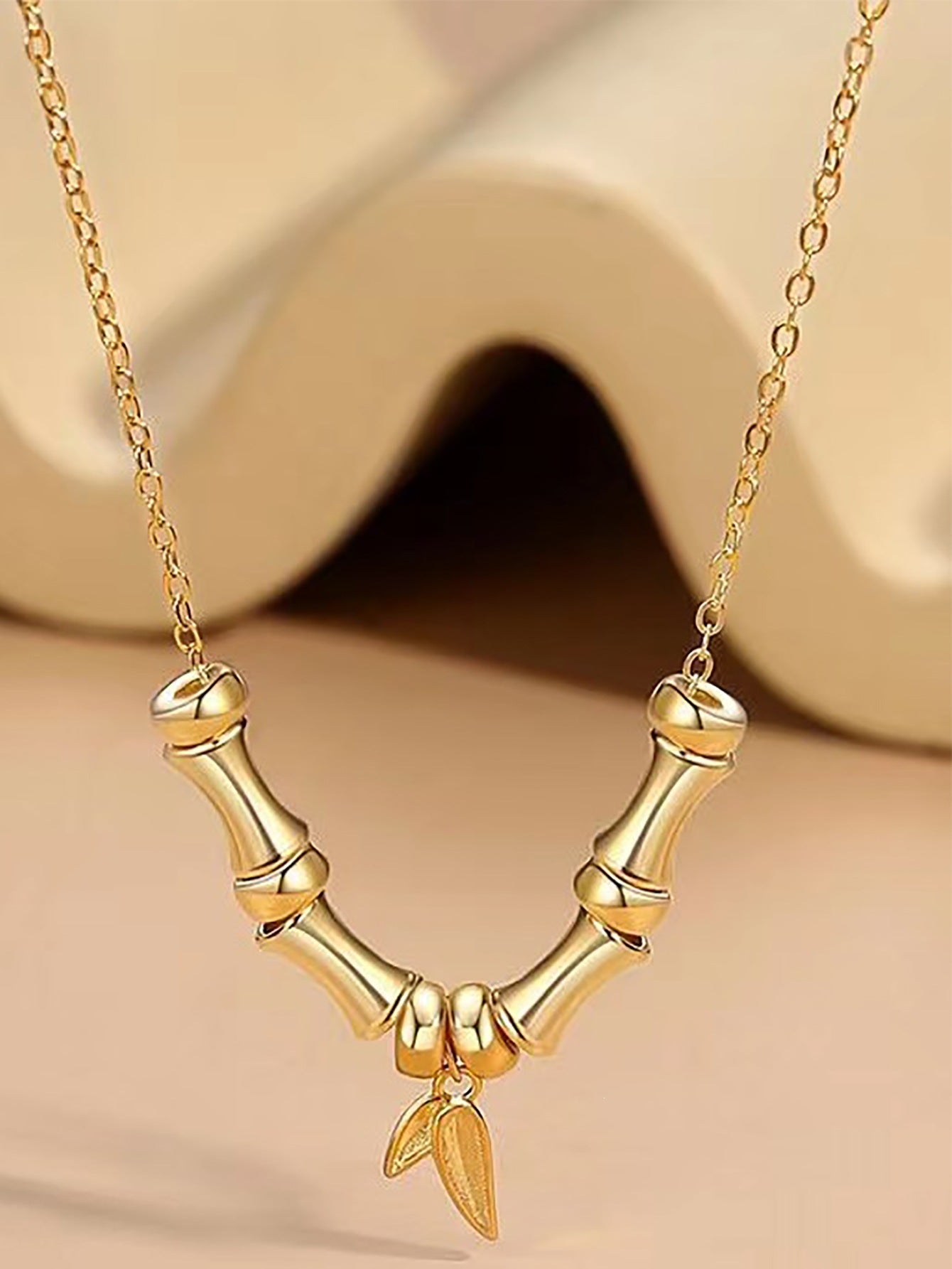 Close-up view of a gold-tone necklace featuring a bamboo branch design with a hanging leaf charm.