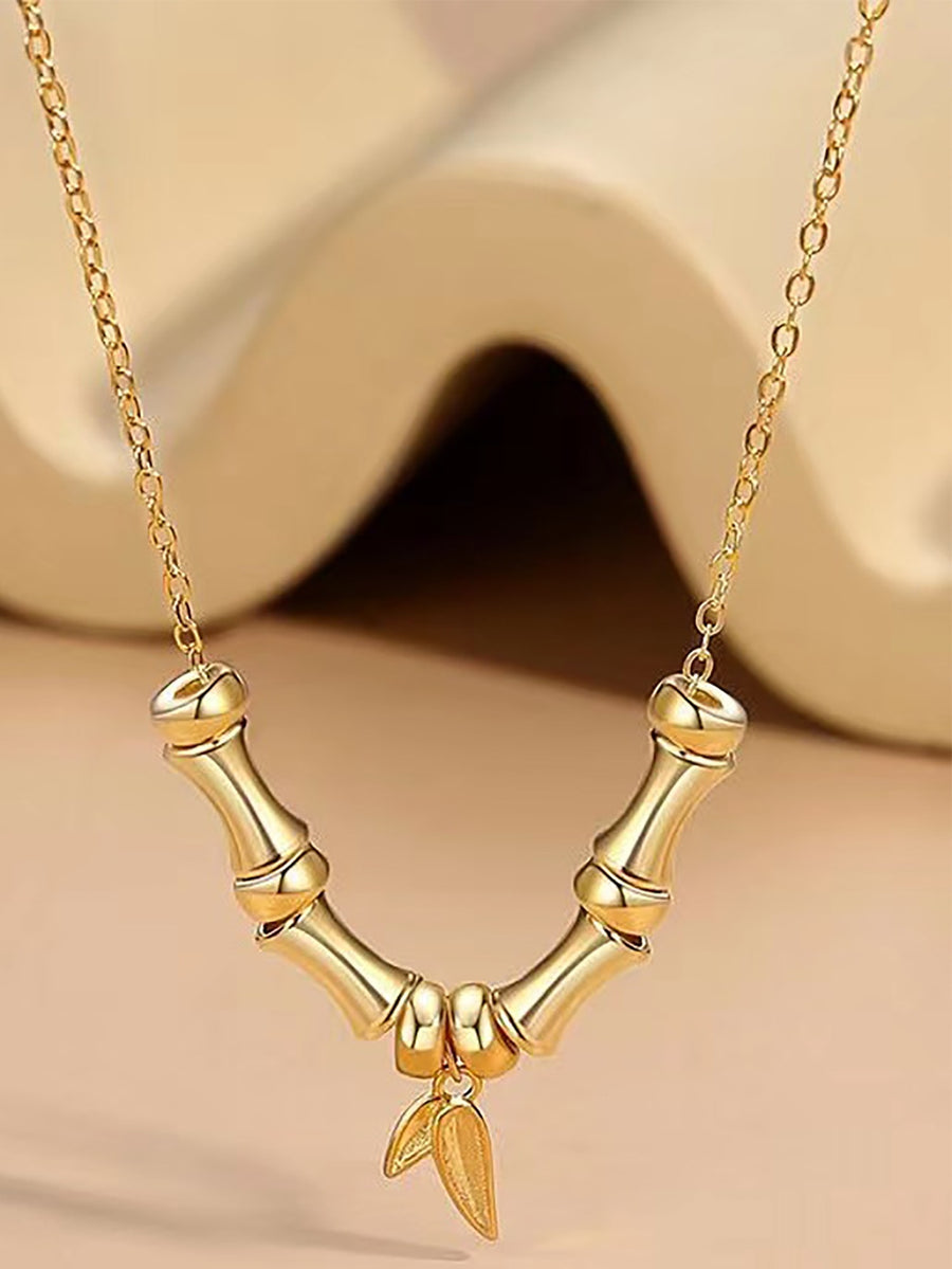 Close-up view of a gold-tone necklace featuring a bamboo branch design with a hanging leaf charm.