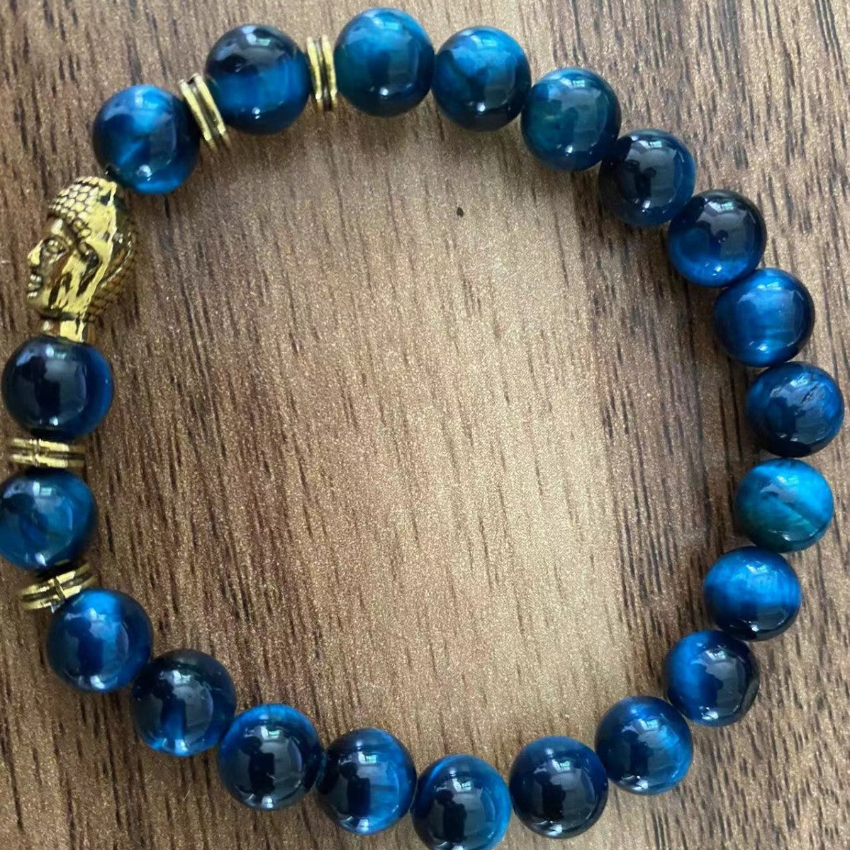 Blue stone bead bracelet with gold Buddha charm on wood surface