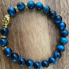Blue stone bead bracelet with gold Buddha charm on wood surface