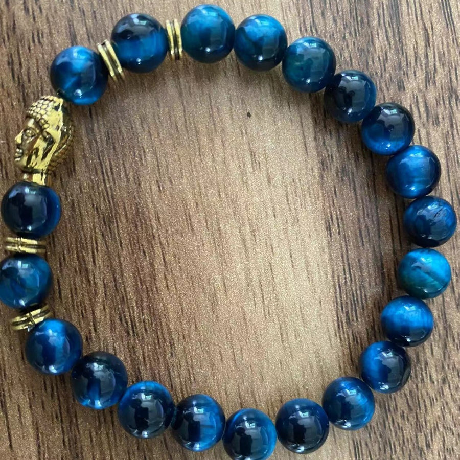 Blue stone bead bracelet with gold Buddha charm on wood surface