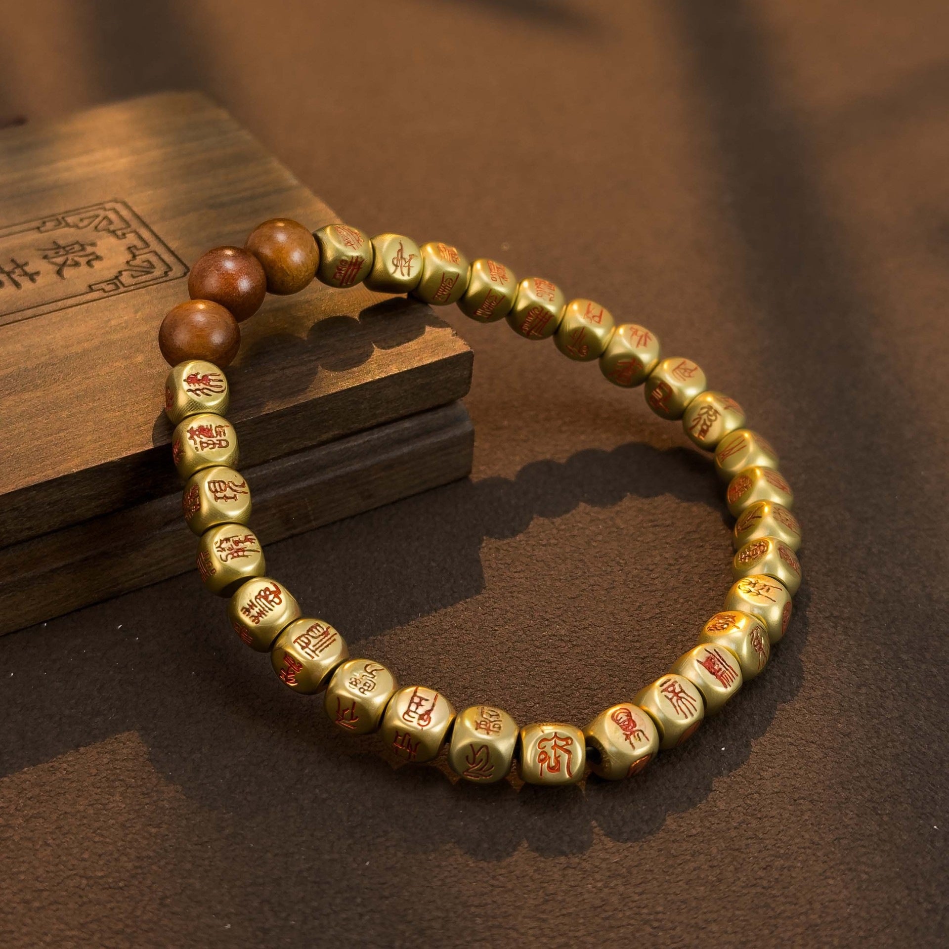 Gold tone copper bracelet with engraved characters and brown cinnabar beads resting on a wooden surface