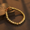 Gold tone copper bracelet with engraved characters and brown cinnabar beads resting on a wooden surface