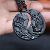 Two crescent shaped black obsidian pendants with dragon and phoenix carvings on a dark background