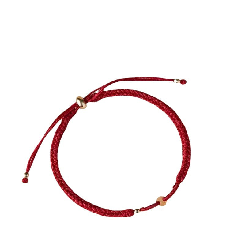 Close up of a red braided cord bracelet with a small gold tone bead.