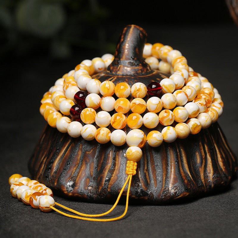 Coiled white and yellow amber 108 bead mala bracelet on a black stone surface