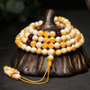 Coiled white and yellow amber 108 bead mala bracelet on a black stone surface