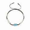 Close up of a braided grey cord bracelet with white beads and a blue carved charm