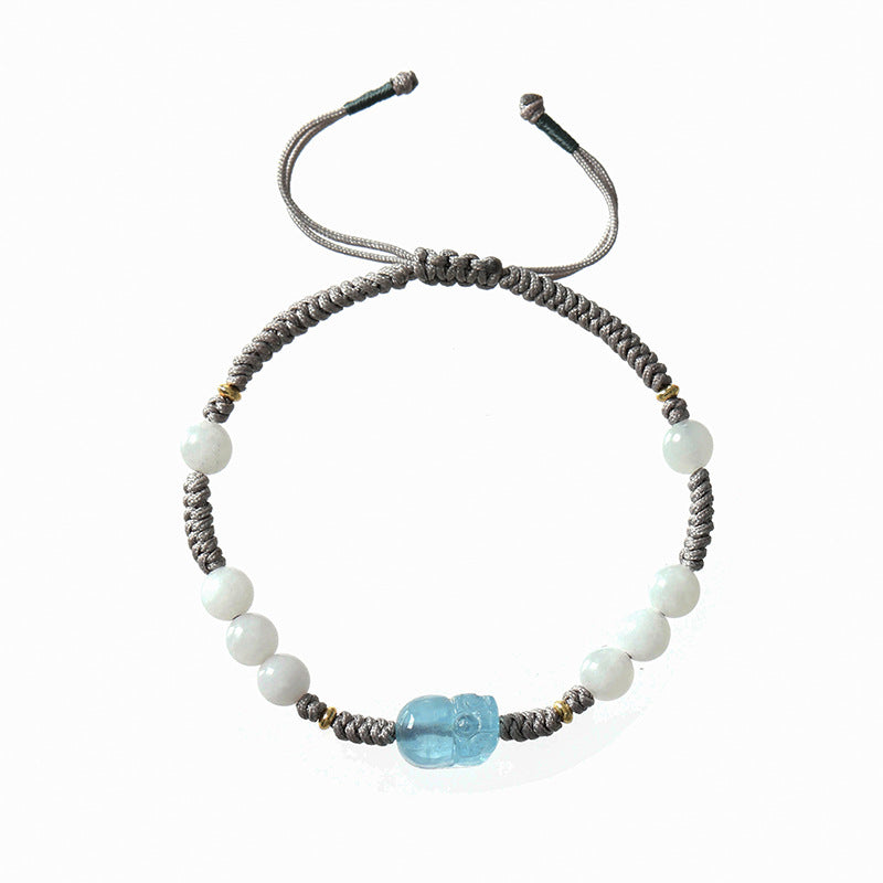 Close up of a braided grey cord bracelet with white beads and a blue carved charm