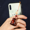 Close up of a dark wood cat phone charm hanging from a smartphone