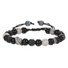 Black and white beaded bracelet with feather charm resting on a dark stone surface