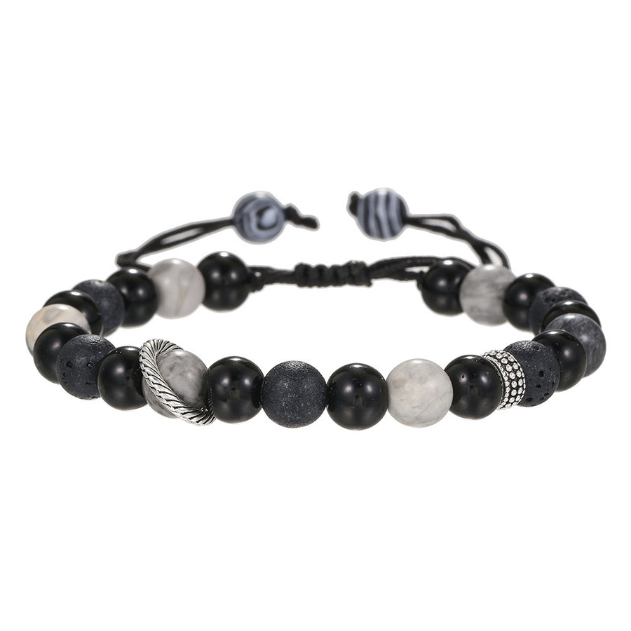 Black and white beaded bracelet with feather charm resting on a dark stone surface