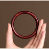 Close up of a smooth reddish brown wooden bangle held in hand