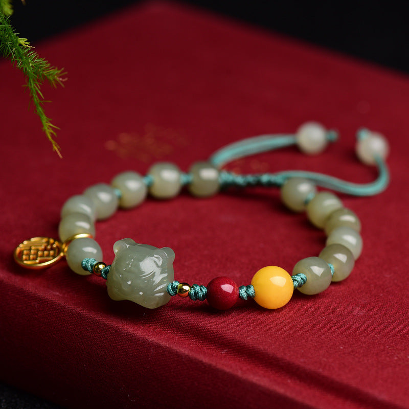 Close up of a light green jade bracelet with a carved tiger charm and red and yellow accent beads