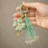 Hand holding a green Song brocade four leaf clover keychain with a matching beaded tassel
