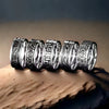 A row of five silver rings with black engraved patterns resting on a stone surface
