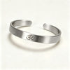 Brushed silver open cuff bracelet with engraved OM symbol on white background