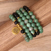 Green and black beaded mala bracelet wrapped around a wrist with a gold lotus charm