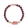 Close up of a beaded bracelet with dark red garnet stones and a pink carved charm on a wrist