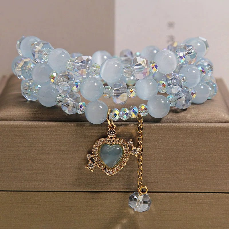 Close up of a blue cat's eye triple wrap bracelet with a gold heart charm