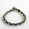 Close-up of a black, white, and gold braided cord bracelet with a metal clasp on a white background.
