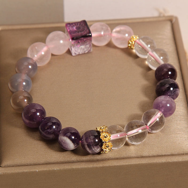 Close-up of a beaded bracelet with purple, pink, and clear crystals on a beige box