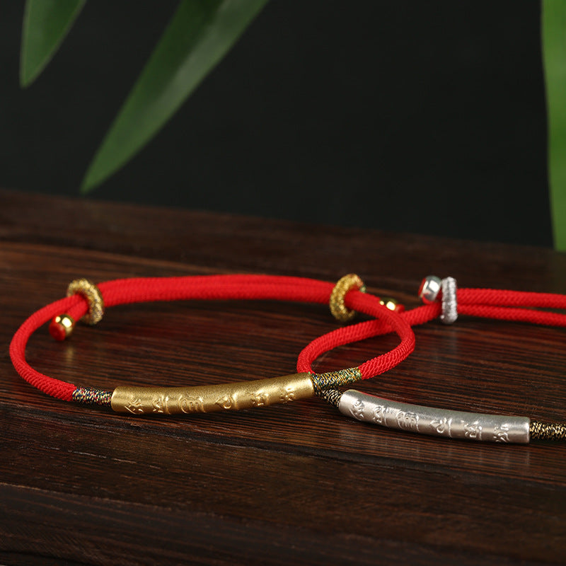 Close up of silver and gold plated bracelets with mantra engraving on red cord