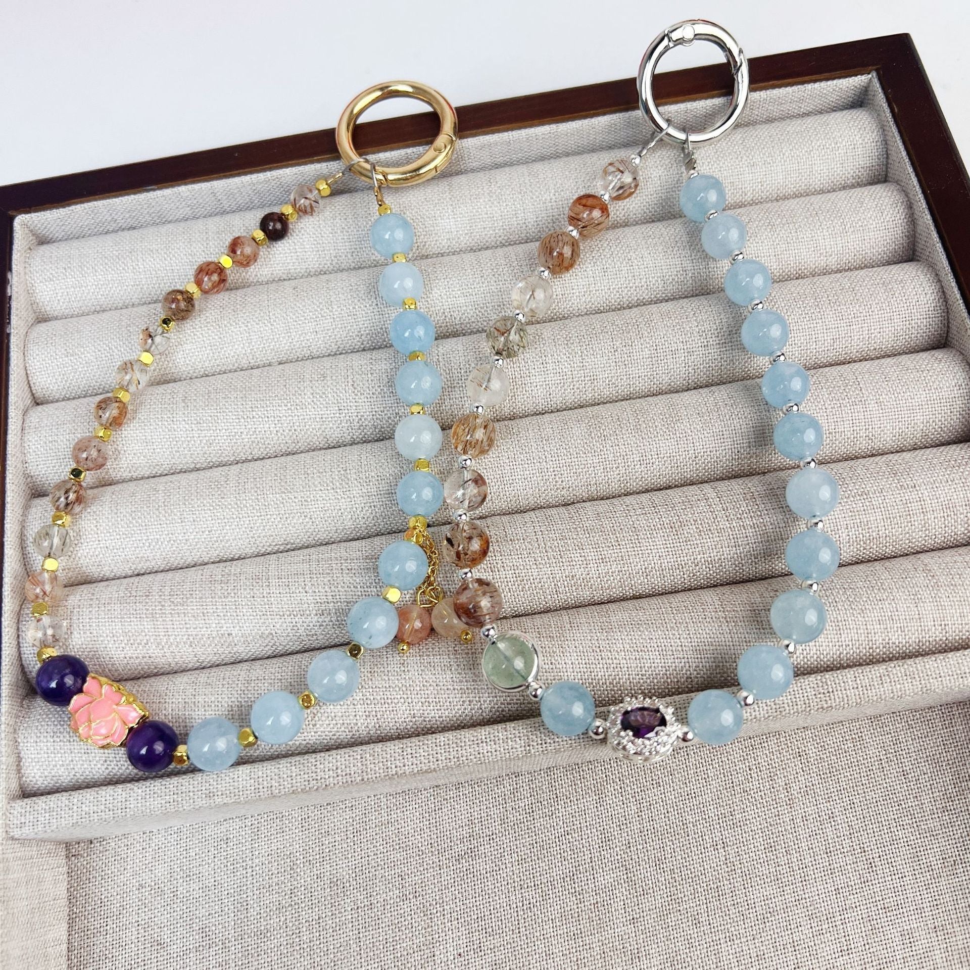 Two beaded crystal phone charms with large metal rings resting on a jewelry display tray