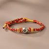 A close-up of a red and gold braided bracelet with a silver-tone charm featuring a Buddhist figure.