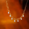 Close-up of a gold-tone multi-strand necklace with hanging pearl beads against a warm background.